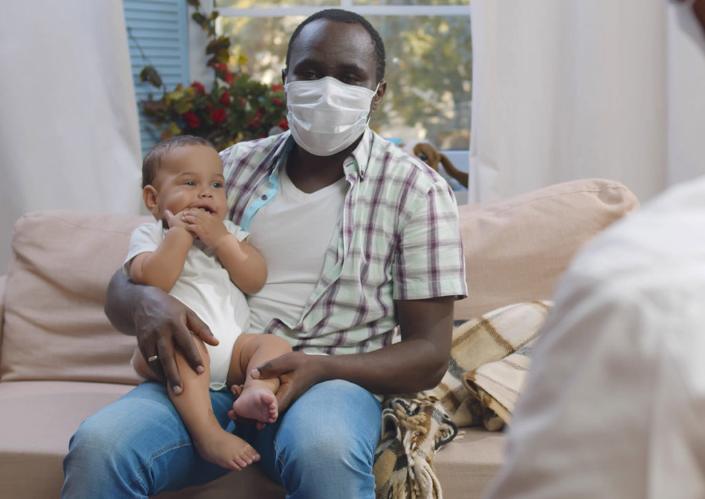 dad in mask holding baby during medical checkup