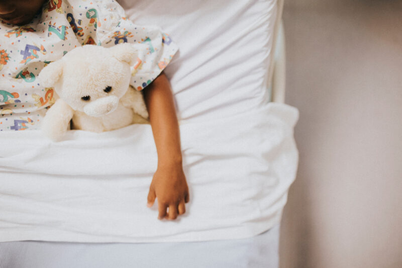 child with white stuffed bear in hospital bed