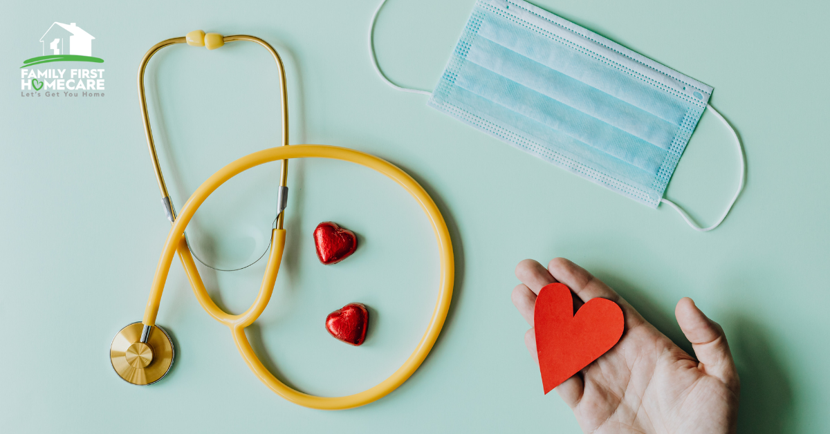 stethoscope, face mask, and hand holding red paper heart on top of blue-green background