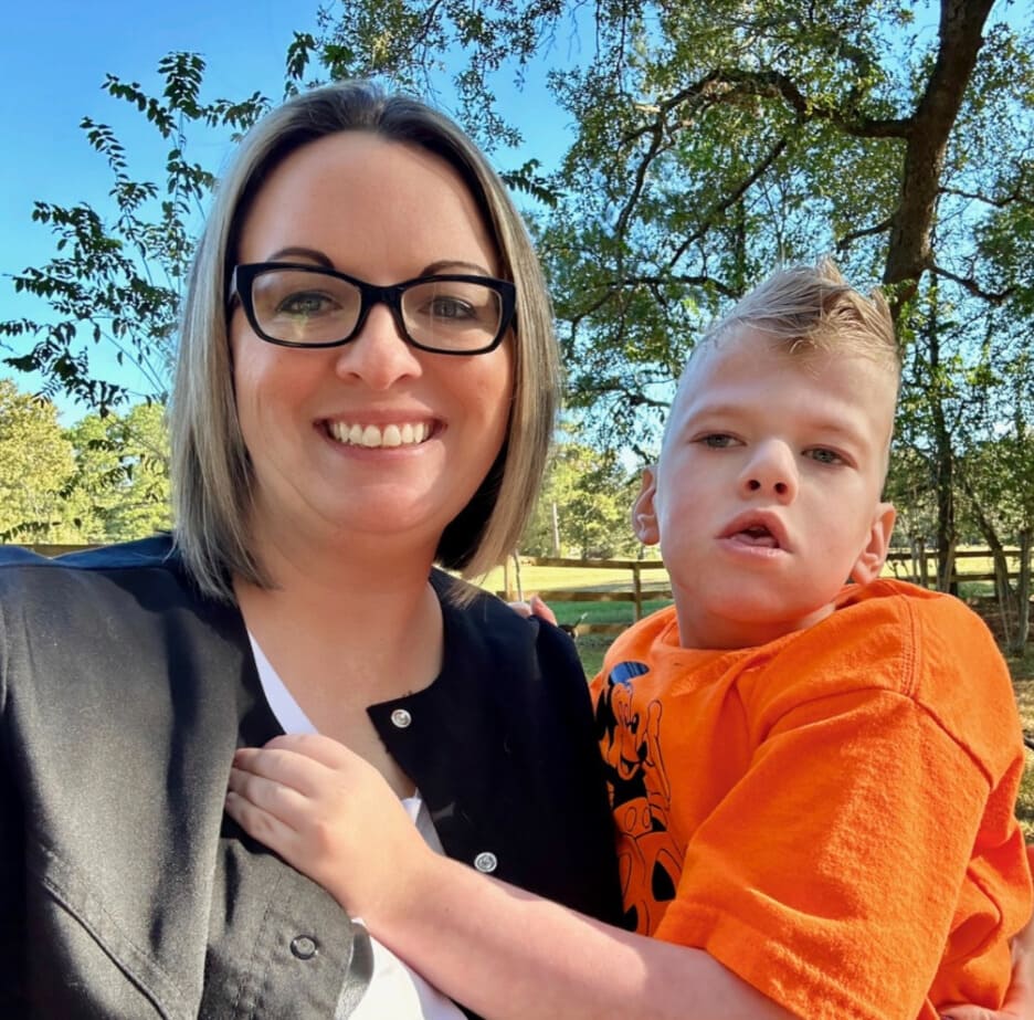 Woman with glasses holding a pediatric homecare patient in her arms under a tree