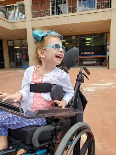 Pediatric care patient with blue glasses in a wheelchair smiling