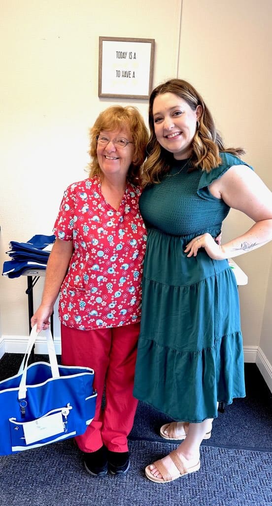 Two women standing and smiling for a picture, one wearing red scrubs the other in a teal dress