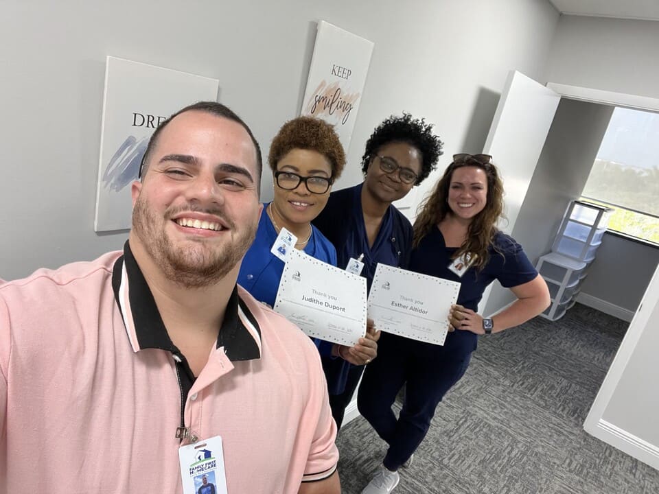 One man in pink and three nurses in blue scrubs stand smiling for a picture, two are holding thank you certificates