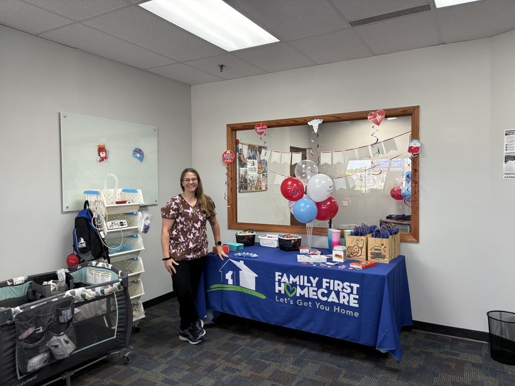 A woman in scrubs standing in front of a Family First Homecare decorated table