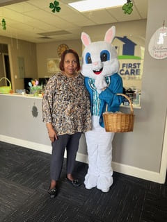 A woman stands and smiles next to the Easter Bunny who is holding a basket