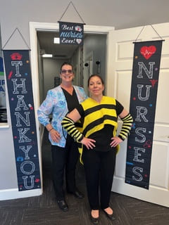 Two woman stand with their hands on their hips smiling at the camera, none is dressed like a bee