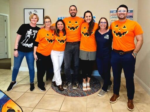 Seven people standing and smiling in Pumpkin, Skeleton, and Family First themed shirts