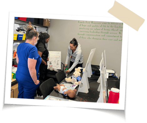 A woman training two nurses on the use of oxygen tanks, they are practicing with a fake baby that sits on the table