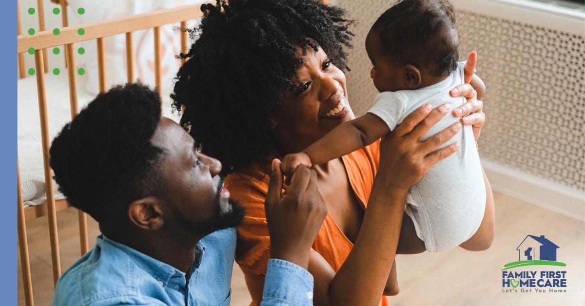 man sitting next to a woman holding a baby with a crib in the background